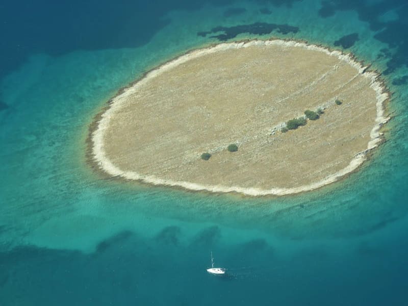 Otočić u tirkiznom moru s usidrenim brodom, snimljen iz zraka
